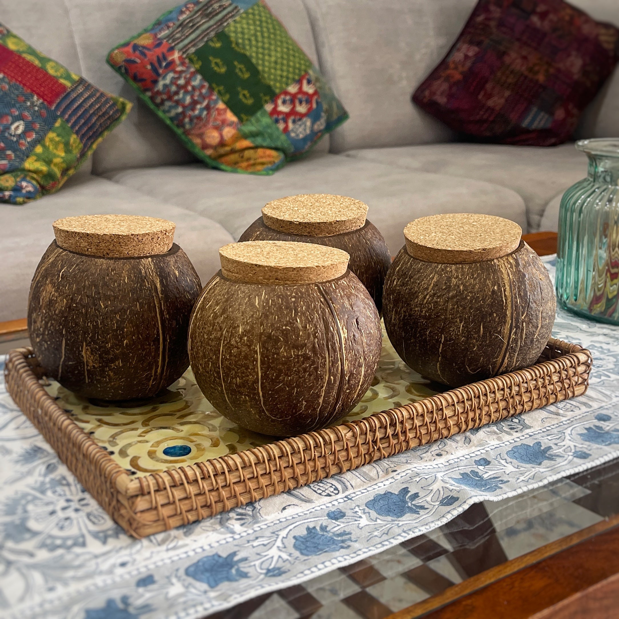 Handcrafted coconut shell jars with cork lids, displayed on a woven tray in a cozy living room setting